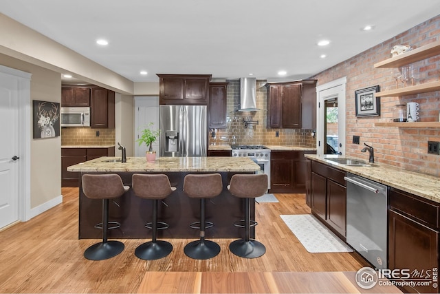 kitchen featuring decorative backsplash, light wood-style floors, wall chimney exhaust hood, a sink, and appliances with stainless steel finishes