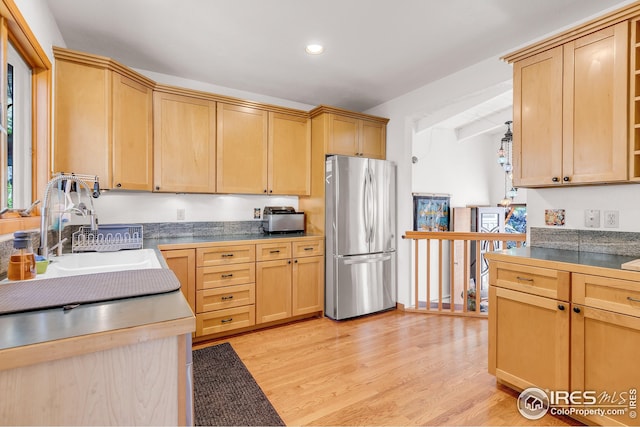 kitchen featuring light wood-type flooring, a sink, freestanding refrigerator, light brown cabinets, and recessed lighting