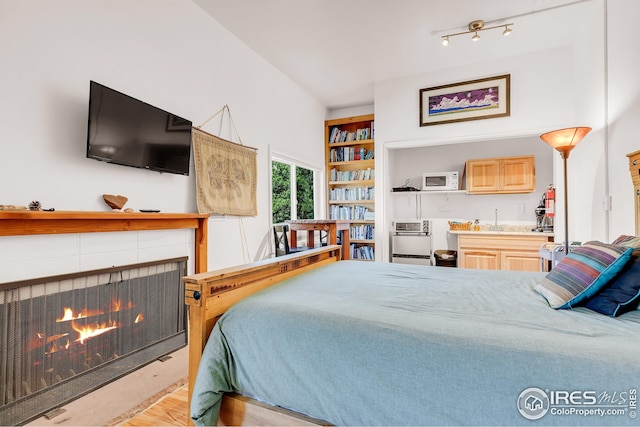 bedroom with a tiled fireplace, a sink, and light wood finished floors