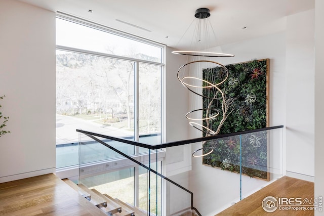 stairway with floor to ceiling windows, wood finished floors, and a notable chandelier
