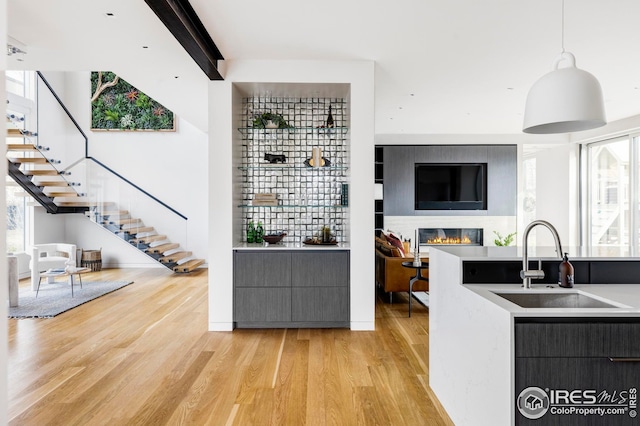 kitchen with a sink, light wood finished floors, light countertops, a glass covered fireplace, and decorative light fixtures