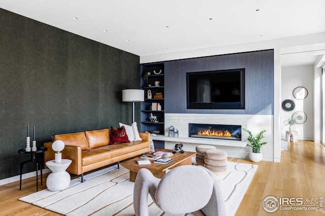 living area featuring baseboards, a glass covered fireplace, built in features, and wood finished floors