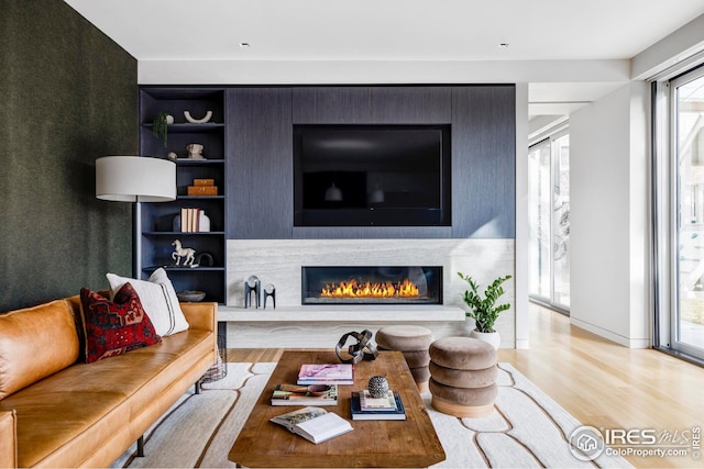 living room with built in features, a glass covered fireplace, and wood finished floors