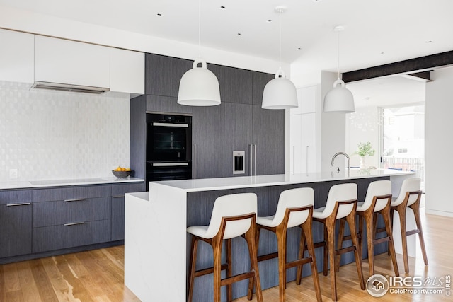 kitchen with dobule oven black, cooktop, light wood-style floors, and modern cabinets