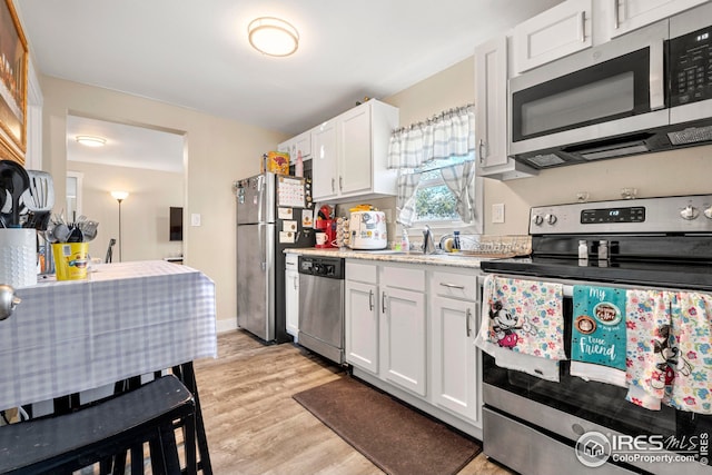 kitchen with appliances with stainless steel finishes, light countertops, a sink, white cabinets, and light wood-style floors