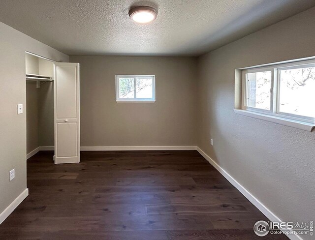 unfurnished bedroom featuring a textured ceiling, baseboards, dark wood finished floors, and a closet