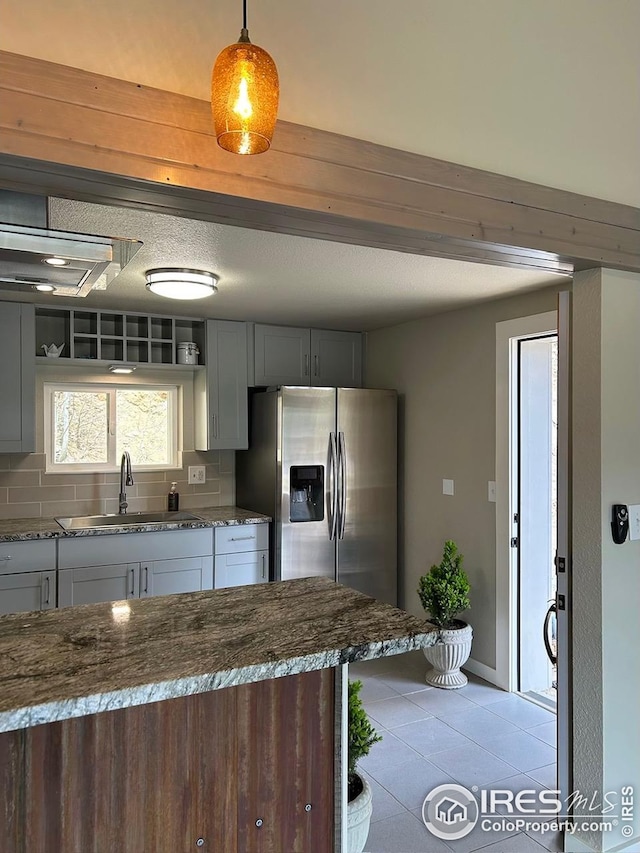 kitchen featuring decorative backsplash, stainless steel refrigerator with ice dispenser, a sink, light tile patterned floors, and dark stone counters