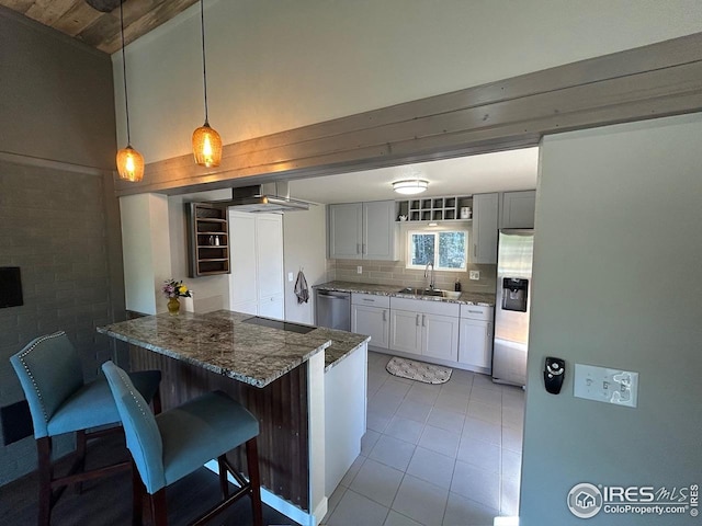 kitchen with appliances with stainless steel finishes, a breakfast bar, a sink, dark stone countertops, and a peninsula