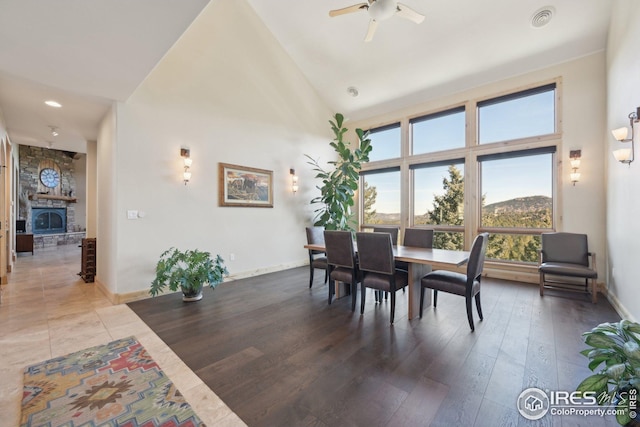 dining space featuring a stone fireplace, a ceiling fan, baseboards, lofted ceiling, and visible vents