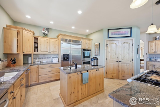 kitchen featuring light brown cabinets, backsplash, stainless steel appliances, and an island with sink