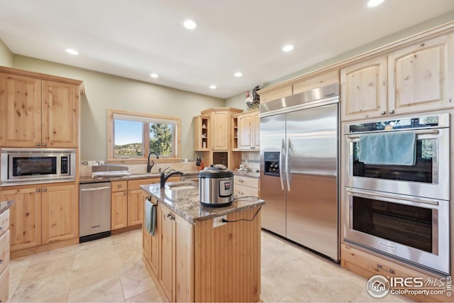 kitchen featuring built in appliances, light brown cabinets, light stone countertops, an island with sink, and recessed lighting
