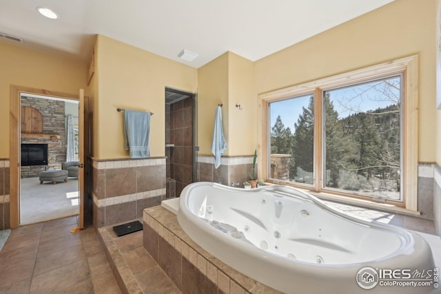 full bathroom with visible vents, a stone fireplace, tile patterned flooring, and a jetted tub