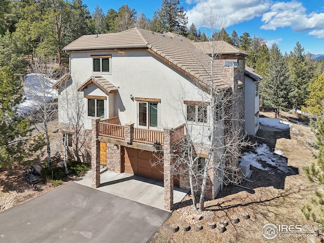 rear view of property featuring stone siding, stucco siding, an attached garage, driveway, and a tile roof