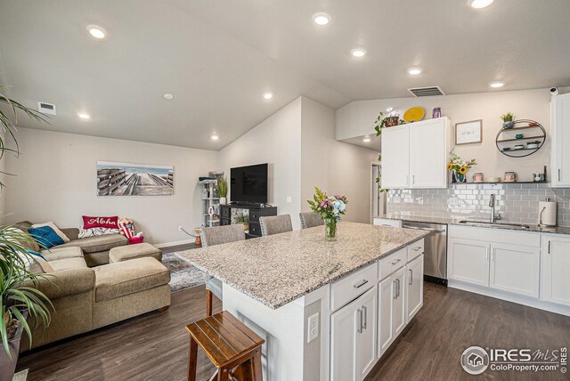 kitchen with a kitchen bar, stainless steel dishwasher, dark wood finished floors, a sink, and open floor plan