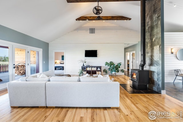 living area with a wood stove, beam ceiling, wood finished floors, wooden walls, and high vaulted ceiling