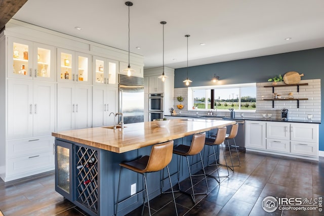 kitchen with a sink, butcher block countertops, stainless steel appliances, white cabinetry, and backsplash
