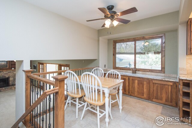 dining area featuring ceiling fan and a stone fireplace