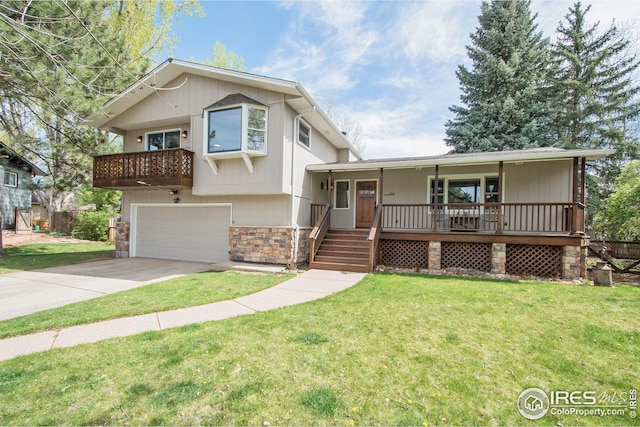 tri-level home with covered porch, concrete driveway, stone siding, and a front lawn