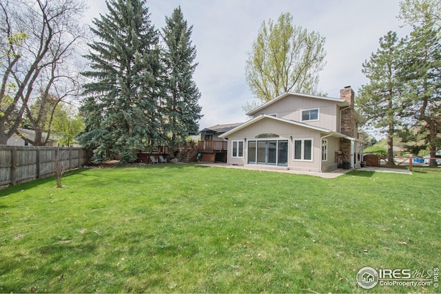 back of property featuring a fenced backyard, a wooden deck, a yard, and a chimney