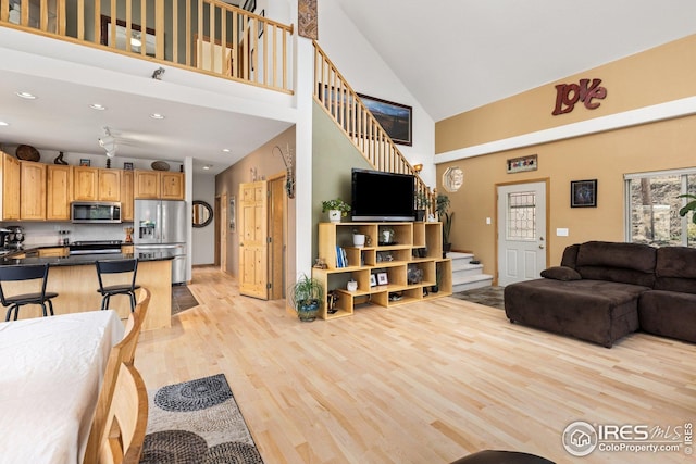 living area featuring light wood-style floors, high vaulted ceiling, recessed lighting, and stairs