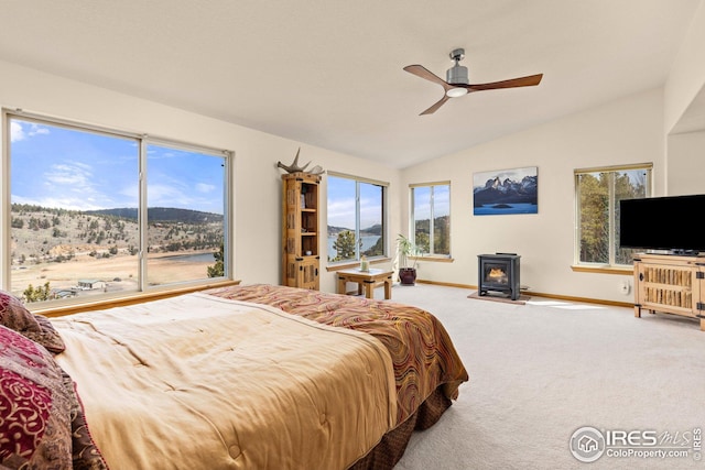 bedroom featuring multiple windows, a wood stove, carpet floors, baseboards, and vaulted ceiling