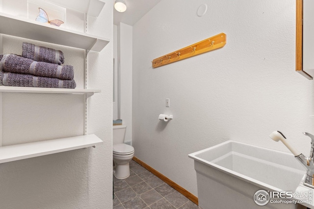 bathroom with toilet, baseboards, and tile patterned flooring