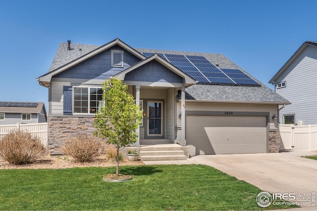 craftsman-style home with fence, a front lawn, stone siding, roof mounted solar panels, and concrete driveway