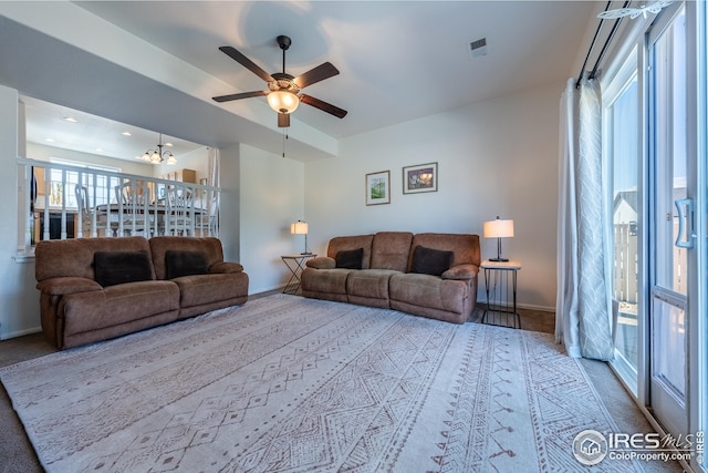 carpeted living room with baseboards, ceiling fan with notable chandelier, and visible vents