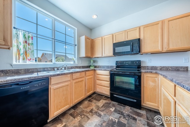 kitchen with stone finish flooring, light brown cabinetry, dark countertops, a sink, and black appliances
