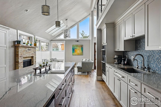 kitchen featuring open floor plan, hardwood / wood-style flooring, a sink, stone counters, and backsplash