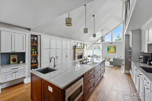 kitchen featuring light wood-style floors, a stone fireplace, light stone counters, a sink, and stainless steel appliances