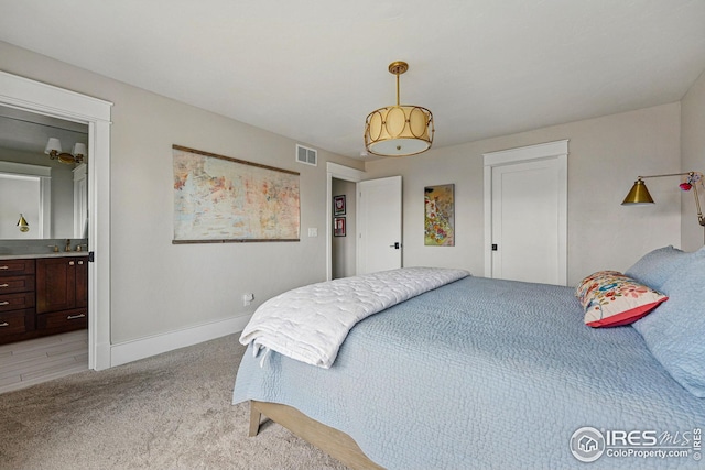 bedroom with baseboards, ensuite bathroom, light carpet, and visible vents
