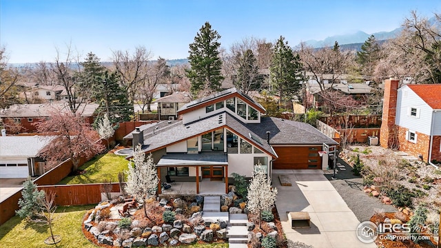 view of front of home with fence, roof with shingles, a residential view, a mountain view, and concrete driveway