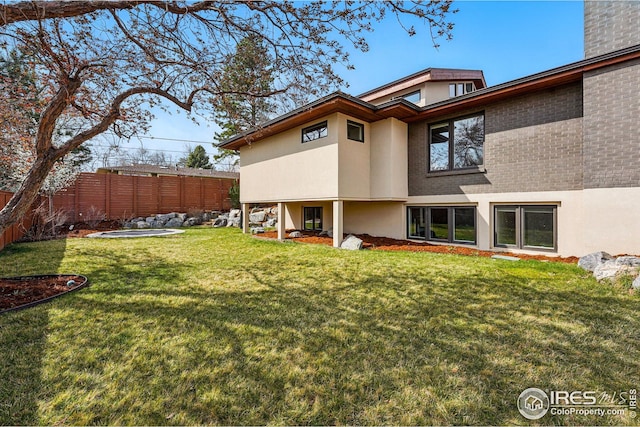 rear view of property with fence, stucco siding, a chimney, brick siding, and a yard