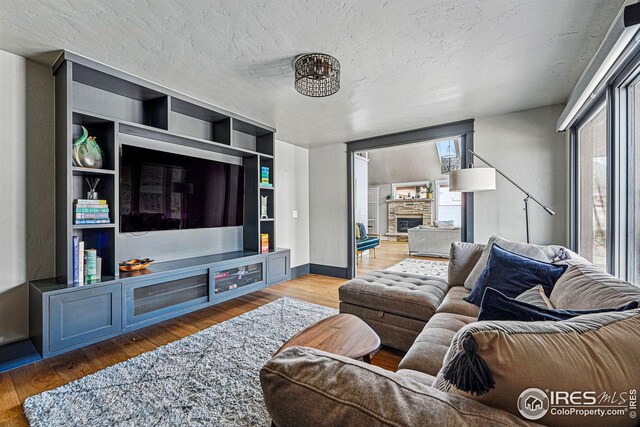 living area with a stone fireplace, a textured ceiling, and wood finished floors