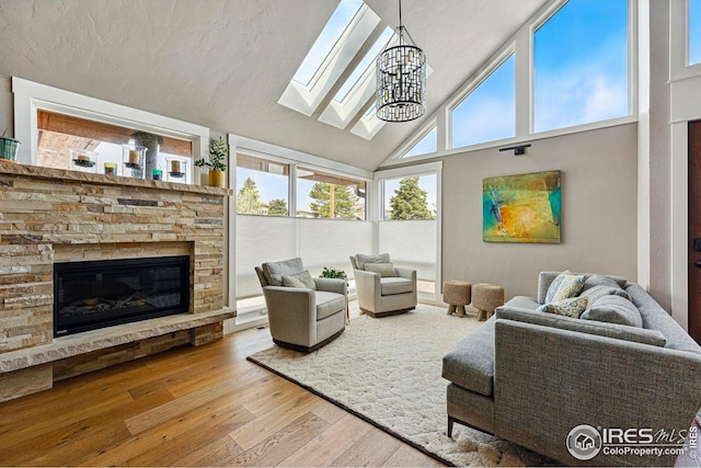 living area with wood-type flooring, an inviting chandelier, a stone fireplace, high vaulted ceiling, and a skylight