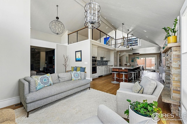 living area featuring an inviting chandelier, a fireplace, high vaulted ceiling, baseboards, and wood finished floors