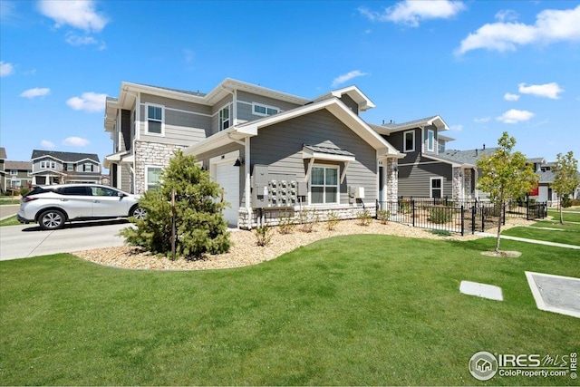 rear view of property with fence, concrete driveway, a yard, and stone siding