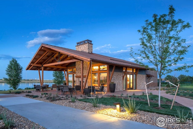 exterior space featuring a water view, a chimney, a patio area, and stone siding