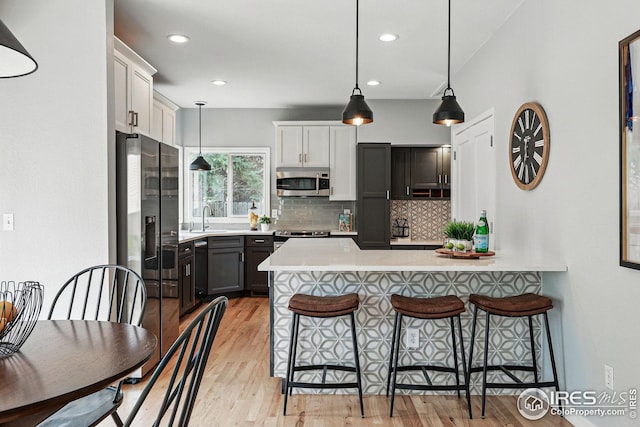 kitchen featuring a sink, a breakfast bar area, stainless steel appliances, a peninsula, and tasteful backsplash