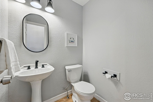 half bathroom with toilet, baseboards, and wood finished floors