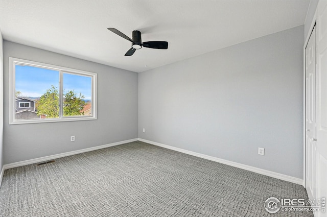 carpeted spare room with visible vents, baseboards, and ceiling fan