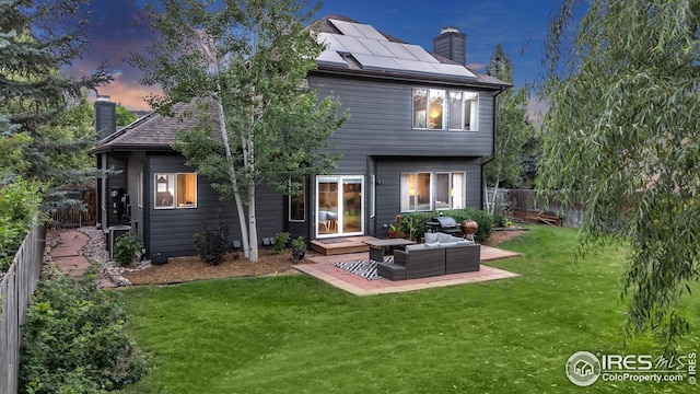 back of house with an outdoor hangout area, roof mounted solar panels, a yard, and a chimney