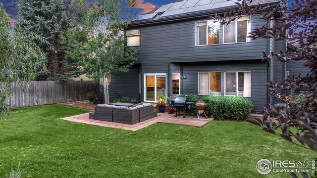 rear view of house featuring fence, a deck, outdoor lounge area, solar panels, and a lawn