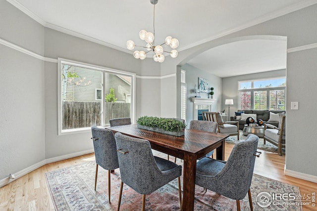 dining area featuring a tiled fireplace, arched walkways, light wood finished floors, and a chandelier