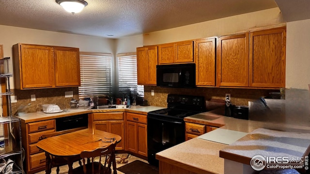kitchen with a textured ceiling, tasteful backsplash, brown cabinets, a sink, and black appliances