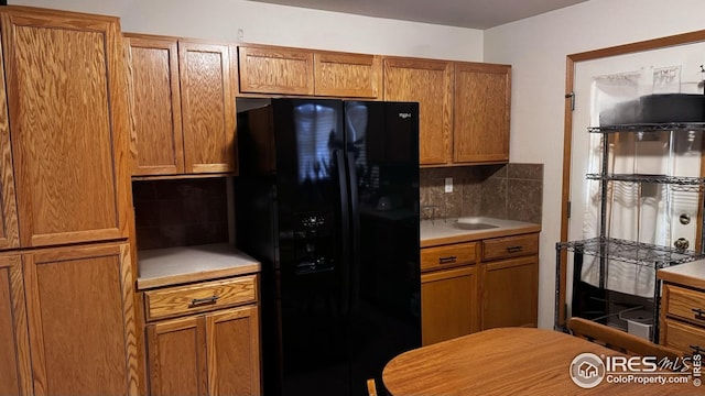 kitchen featuring black fridge with ice dispenser, light countertops, backsplash, and brown cabinets
