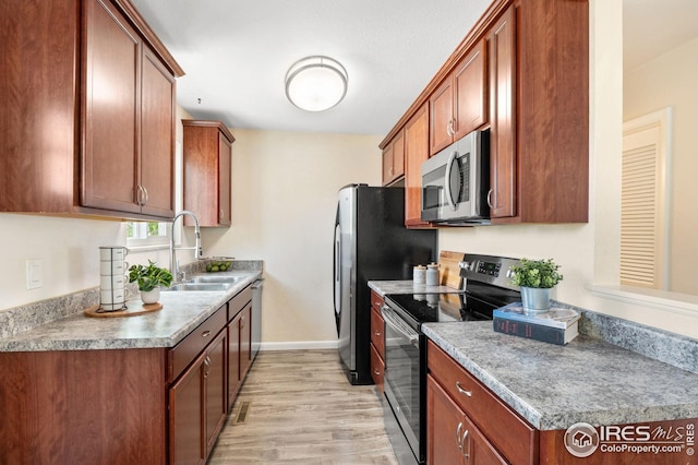 kitchen with appliances with stainless steel finishes, a sink, brown cabinetry, light wood-style flooring, and baseboards