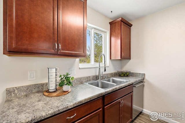 kitchen featuring a sink, light countertops, baseboards, wood finished floors, and stainless steel dishwasher