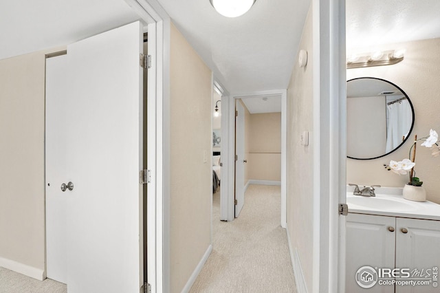 hall with a sink, baseboards, and light colored carpet